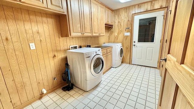 laundry room with light tile patterned floors, washer and clothes dryer, cabinets, and wood walls