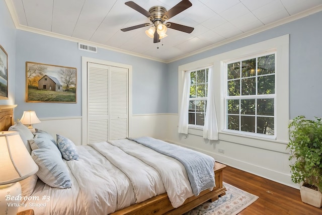 bedroom featuring crown molding, a closet, visible vents, a wainscoted wall, and wood finished floors