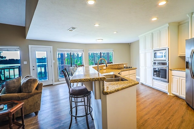 232 Cove Ln, Brookeland, TX 75931 - kitchen with appliances with stainless steel finishes, a sink, wood finished floors, a breakfast bar area, and a kitchen island with sink