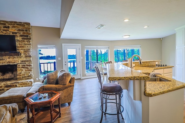 232 Cove Ln, Brookeland, TX 75931 - kitchen featuring open floor plan, wood finished floors, light stone counters, a large island, and a stone fireplace