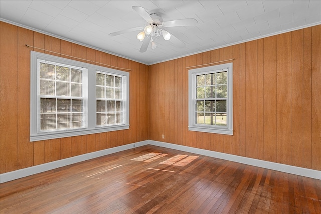 empty room featuring wood-type flooring, ceiling fan, ornamental molding, and wood walls