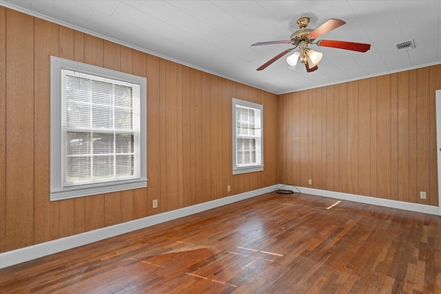 empty room with ceiling fan, wood-type flooring, ornamental molding, and wooden walls