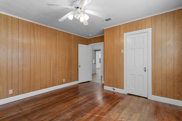 unfurnished bedroom with dark hardwood / wood-style flooring, ceiling fan, ornamental molding, and wood walls