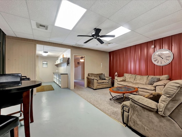 living room with a paneled ceiling, ceiling fan, and concrete flooring