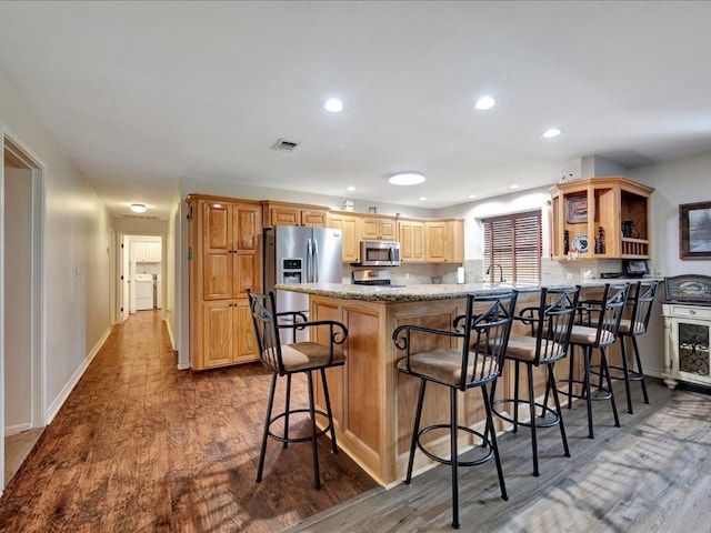 kitchen featuring a kitchen bar, kitchen peninsula, light stone counters, stainless steel appliances, and hardwood / wood-style flooring