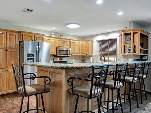 kitchen featuring a kitchen bar, appliances with stainless steel finishes, dark hardwood / wood-style flooring, kitchen peninsula, and tasteful backsplash