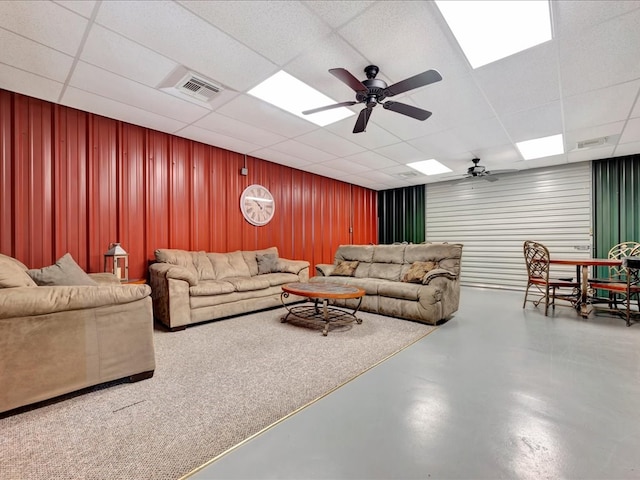 living room with ceiling fan, a drop ceiling, and concrete floors