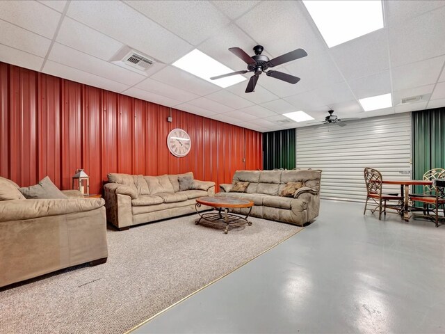 living room with ceiling fan, a drop ceiling, and concrete floors