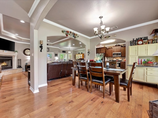166 White Oak Ln, Lufkin, TX 75904 - dining room featuring a chandelier, light wood-style floors, a lit fireplace, arched walkways, and ornamental molding