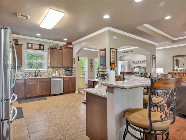 166 White Oak Ln, Lufkin, TX 75904 - kitchen with appliances with stainless steel finishes, a kitchen breakfast bar, arched walkways, backsplash, and light stone countertops