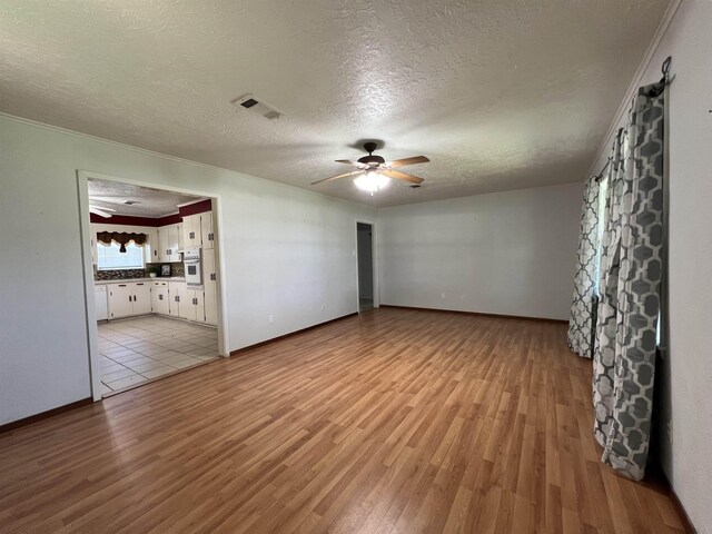 unfurnished living room with ceiling fan, light hardwood / wood-style floors, ornamental molding, and a textured ceiling