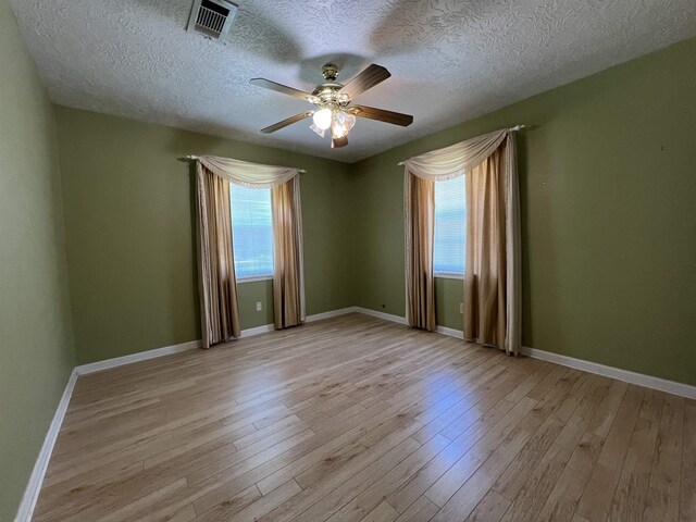 spare room featuring plenty of natural light, ceiling fan, light wood-type flooring, and a textured ceiling