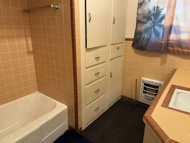 bathroom featuring heating unit, vanity, tile walls, and tiled shower / bath