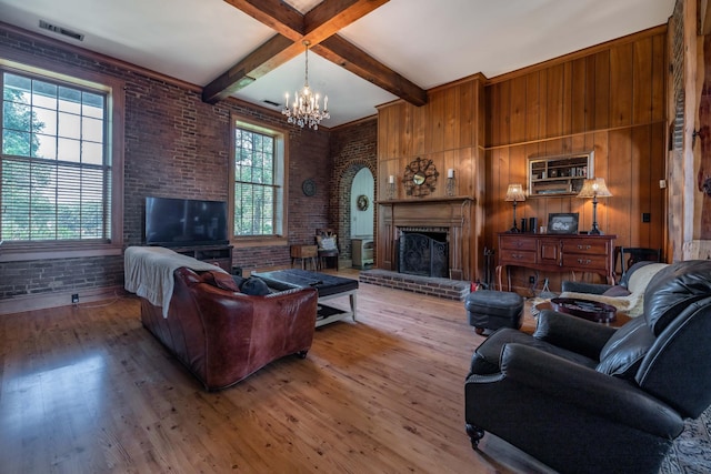 living room with a notable chandelier, beam ceiling, a fireplace, brick wall, and light hardwood / wood-style flooring