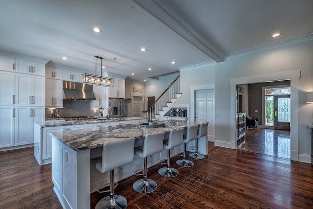 kitchen with hanging light fixtures, stainless steel fridge, a kitchen bar, fume extractor, and a kitchen island with sink