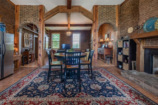 dining area with an inviting chandelier, beam ceiling, a fireplace, brick wall, and a high ceiling