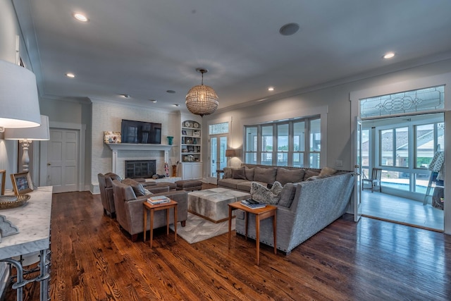 living room featuring built in features, ornamental molding, dark wood-type flooring, and a large fireplace