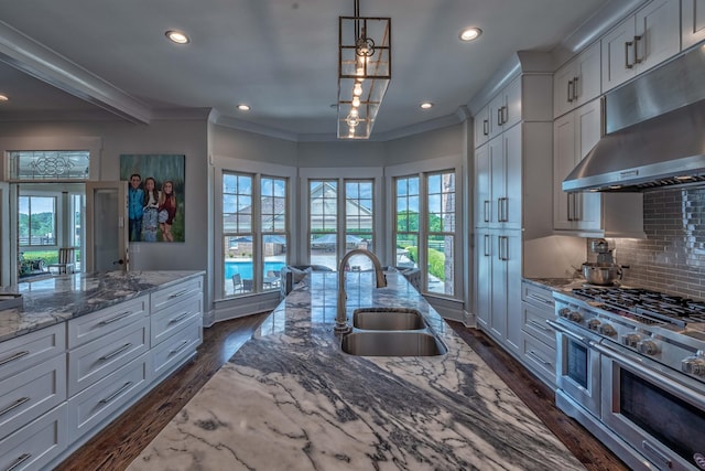 kitchen with tasteful backsplash, sink, light stone countertops, range with two ovens, and hanging light fixtures