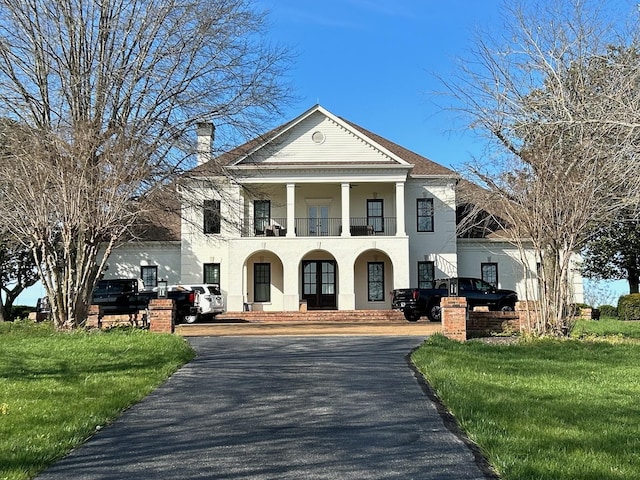 neoclassical / greek revival house featuring a balcony, a front lawn, and french doors