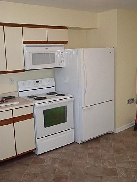 kitchen with white cabinets, white appliances, and dark tile flooring