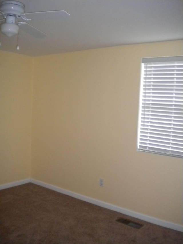 empty room with dark carpet, ceiling fan, and a healthy amount of sunlight