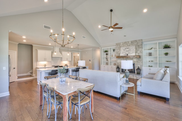 dining area featuring a fireplace, built in shelves, high vaulted ceiling, ceiling fan with notable chandelier, and dark hardwood / wood-style flooring