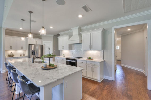 kitchen with dark wood-type flooring, backsplash, custom range hood, appliances with stainless steel finishes, and a center island with sink