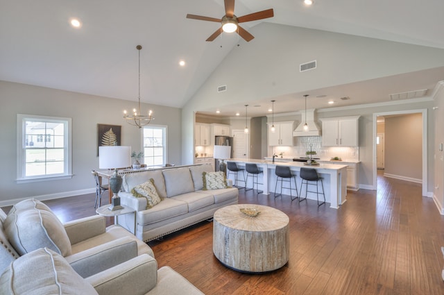 living room with ceiling fan with notable chandelier, dark hardwood / wood-style flooring, and high vaulted ceiling