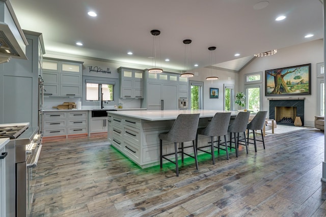 kitchen with dark hardwood / wood-style floors, pendant lighting, a center island, wall chimney exhaust hood, and a kitchen breakfast bar