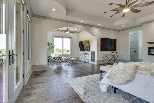 living room featuring ornamental molding, a raised ceiling, dark wood-type flooring, and ceiling fan with notable chandelier