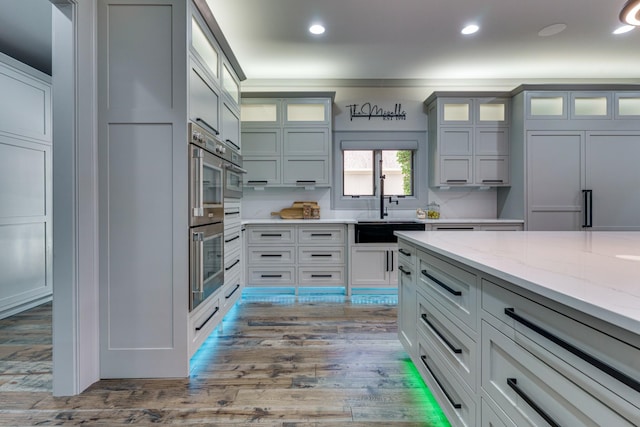 kitchen featuring stainless steel double oven, sink, light hardwood / wood-style floors, and light stone countertops