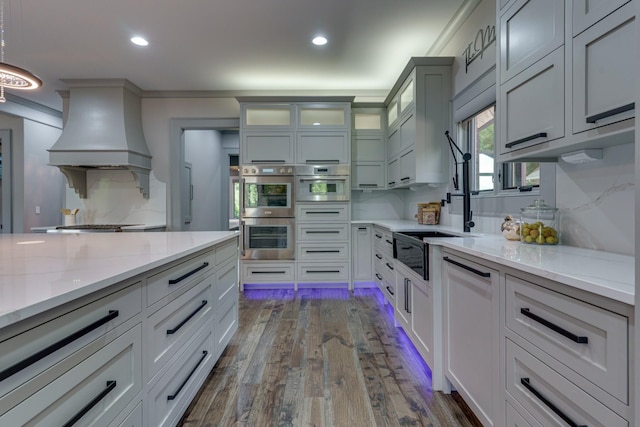 kitchen with stainless steel double oven, light stone countertops, premium range hood, and dark hardwood / wood-style floors