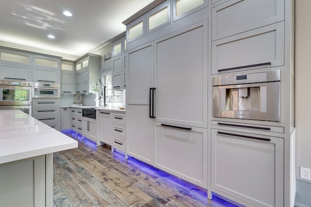 kitchen with stainless steel double oven, light wood-type flooring, and light stone counters