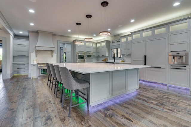 kitchen featuring hanging light fixtures, wood-type flooring, premium range hood, a kitchen bar, and a large island