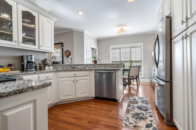 kitchen featuring dark wood-type flooring, stainless steel appliances, light stone countertops, ornamental molding, and white cabinets