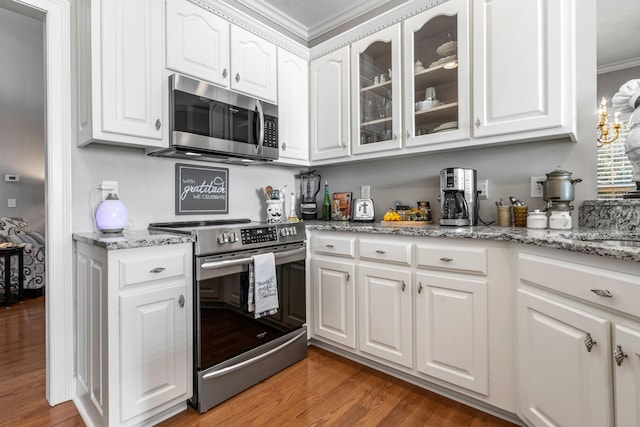 kitchen with appliances with stainless steel finishes, white cabinetry, crown molding, and hardwood / wood-style floors