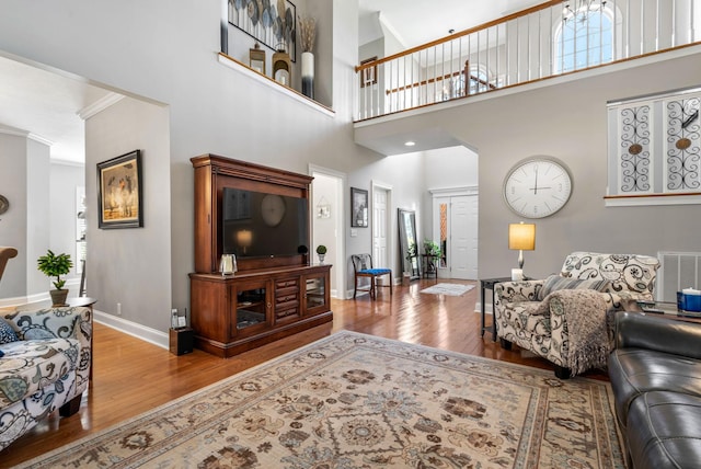 living room with a towering ceiling, ornamental molding, a notable chandelier, and light wood-type flooring