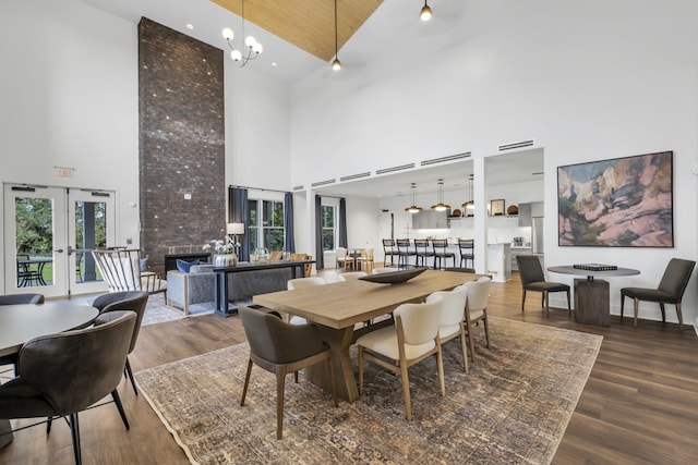 dining area featuring hardwood / wood-style flooring, a towering ceiling, a chandelier, and french doors