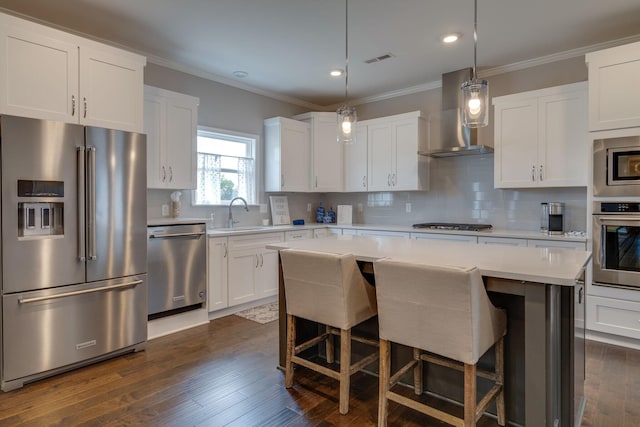 kitchen with wall chimney exhaust hood, visible vents, appliances with stainless steel finishes, light countertops, and a sink