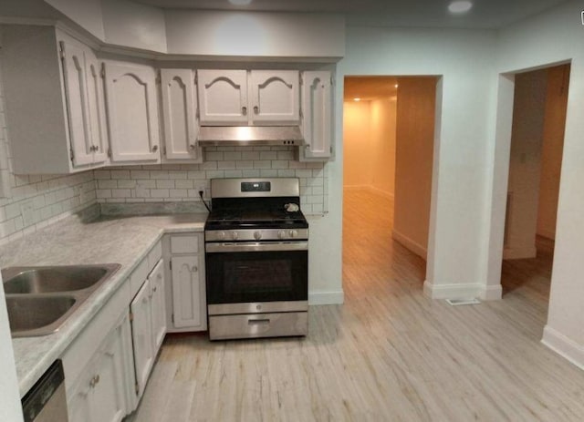 kitchen with appliances with stainless steel finishes, backsplash, white cabinets, and light hardwood / wood-style floors