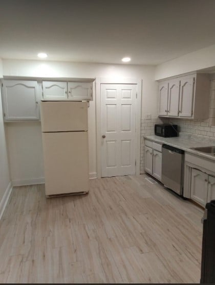 kitchen with white cabinets, white fridge, stainless steel dishwasher, and light hardwood / wood-style floors