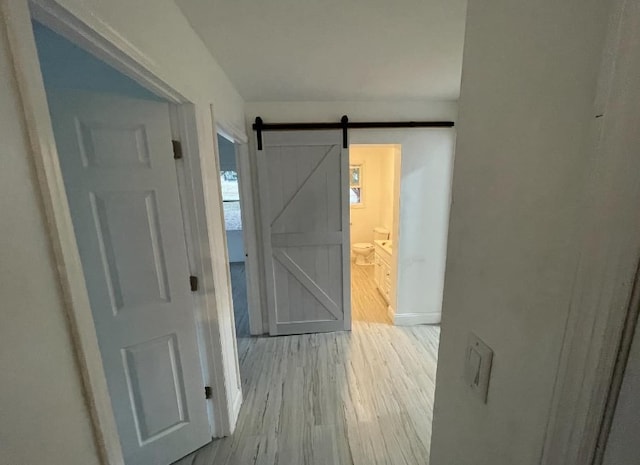 corridor with a barn door and light hardwood / wood-style floors