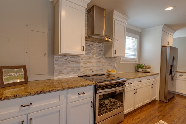 kitchen featuring wall chimney range hood, light stone countertops, white cabinetry, appliances with stainless steel finishes, and light wood-type flooring