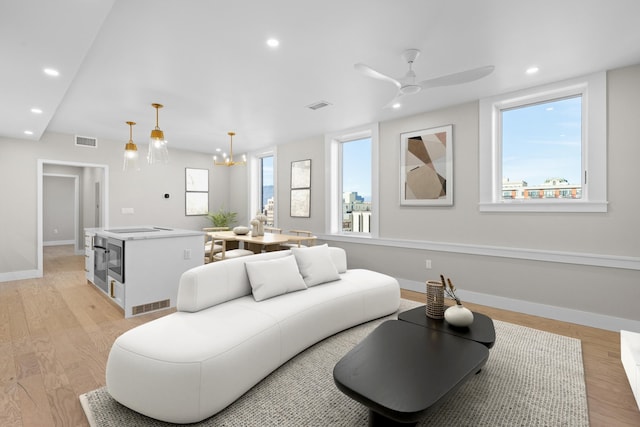 living room with ceiling fan with notable chandelier and light hardwood / wood-style flooring