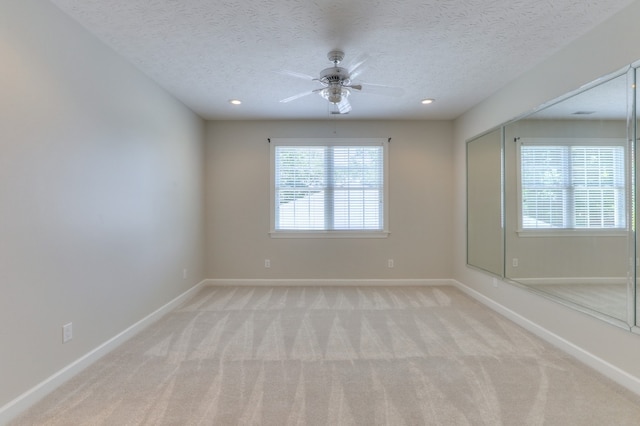 unfurnished room with light colored carpet, ceiling fan, and a textured ceiling