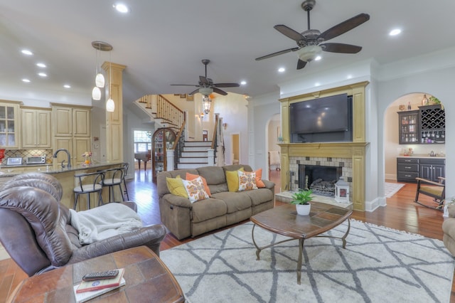 living room featuring a tiled fireplace, ceiling fan, sink, and hardwood / wood-style floors