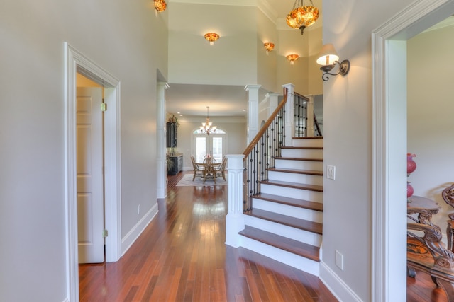 staircase featuring an inviting chandelier, dark hardwood / wood-style floors, decorative columns, and a high ceiling