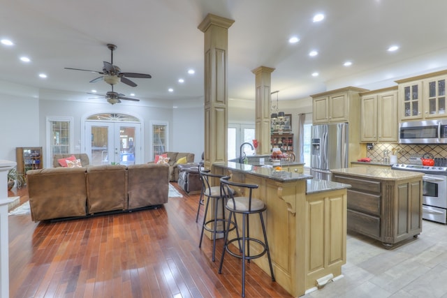 kitchen with french doors, dark stone counters, appliances with stainless steel finishes, ornate columns, and a center island