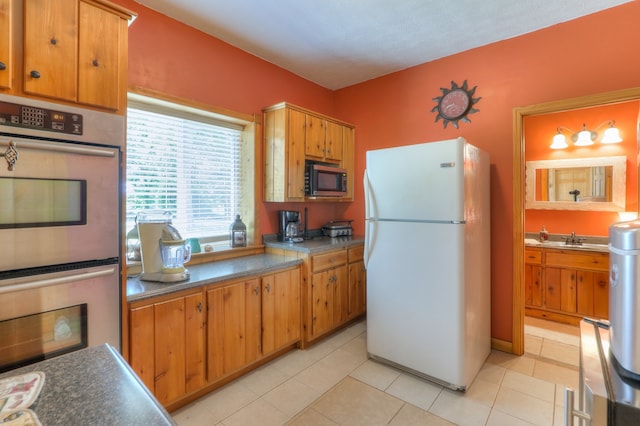 kitchen with sink, white refrigerator, stainless steel double oven, light tile flooring, and black microwave