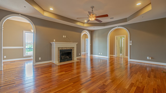 unfurnished living room featuring ceiling fan, a fireplace, hardwood / wood-style flooring, and a raised ceiling